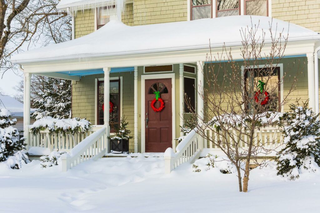 A house with a red door and a wreath on it is covered in snow.