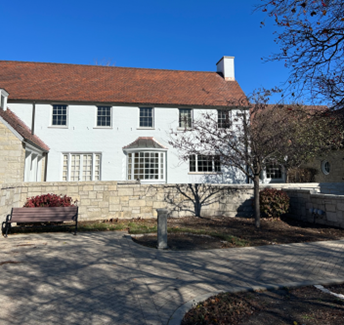 A two-story brick mansion with white columns, a large triangular pediment, and black shutters, set among trees and shrubs.