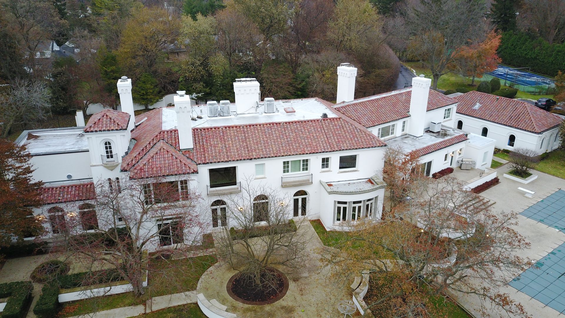 An aerial view of a large white house with a red tile roof surrounded by trees.