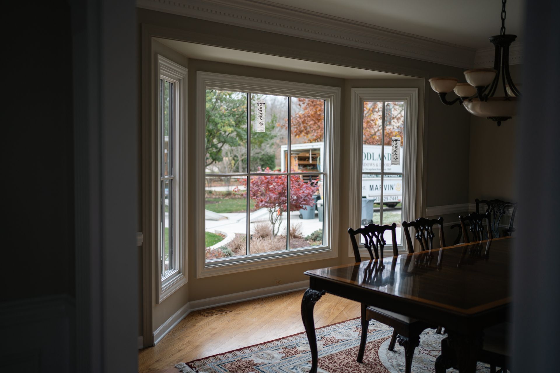 Bay window in dining room with a table and chairs, looking out at a yard with trees.