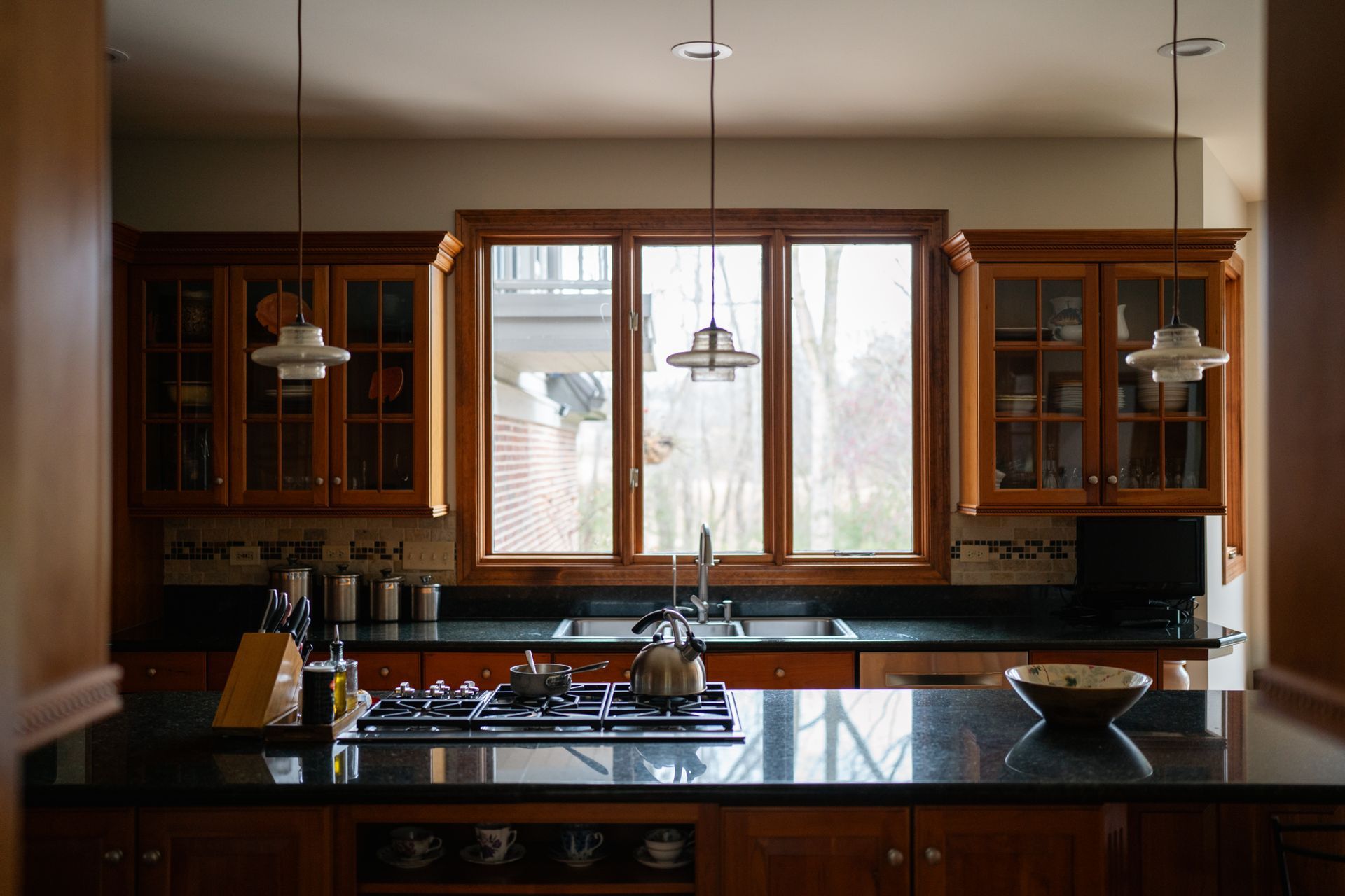 Kitchen with wooden cabinets, black countertops, and a window over the sink, with hanging pendant lights.