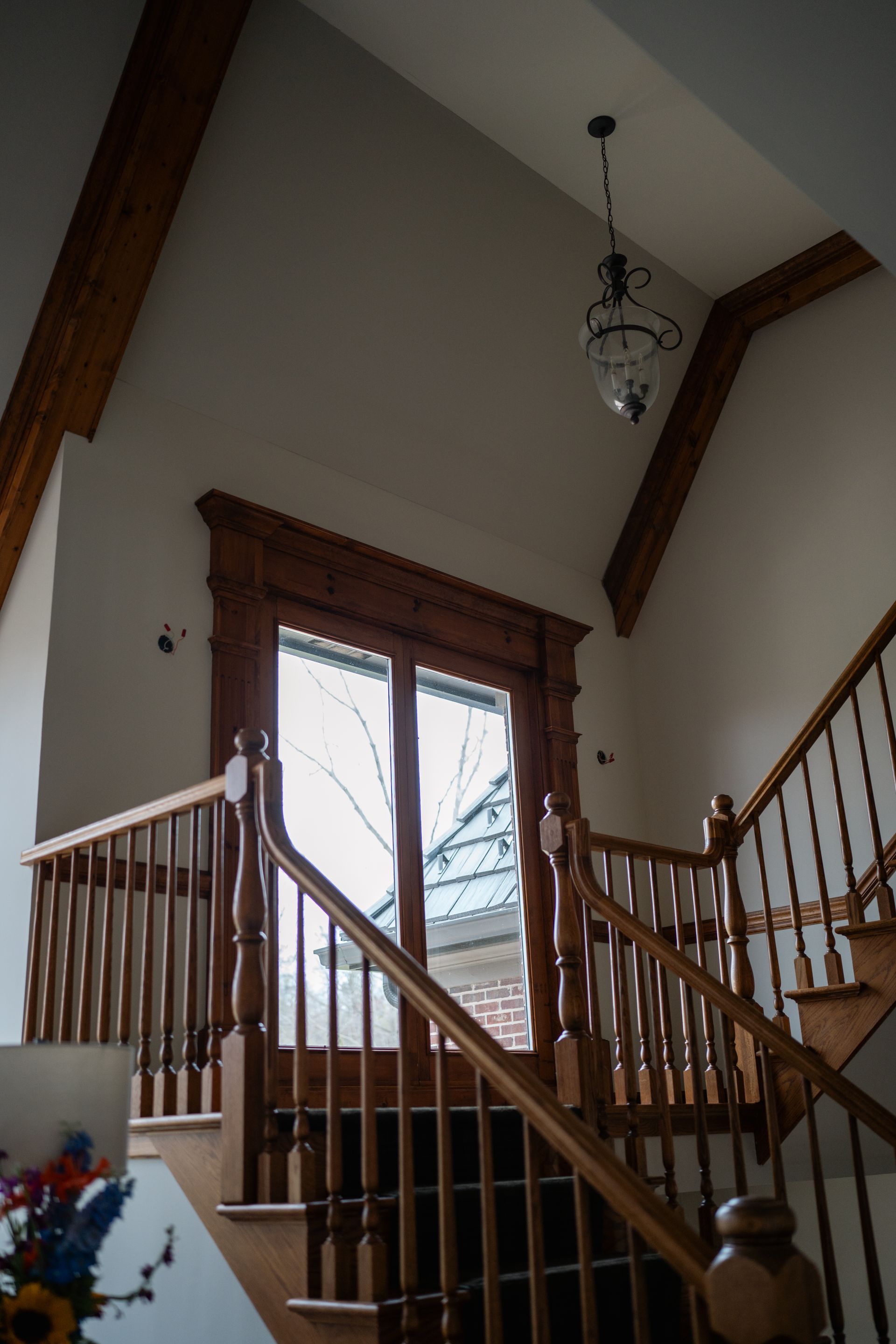 Staircase with wooden banister and window, high ceiling, light fixture.