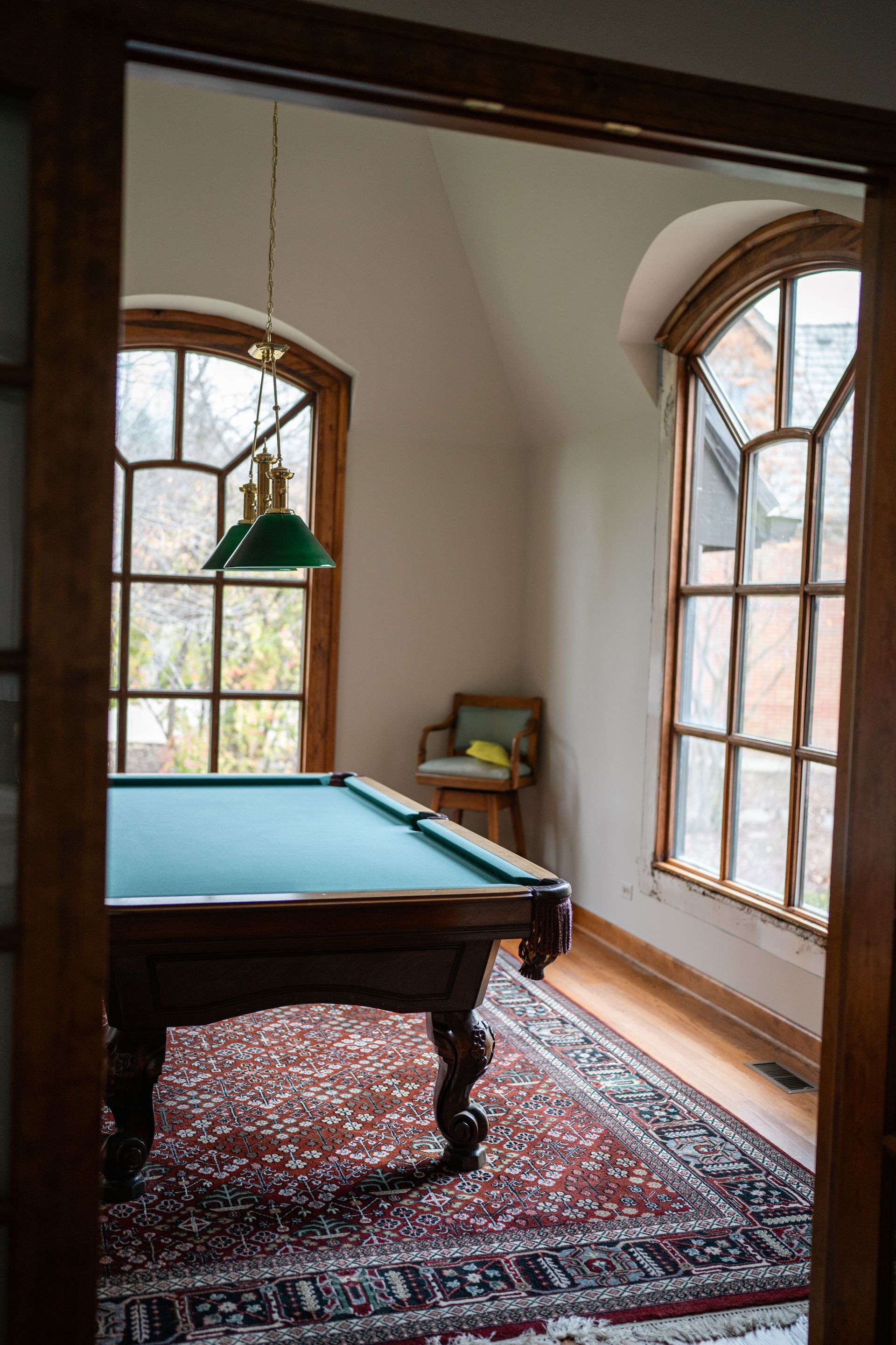 Pool table in a room with large arched windows; green felt, ornate rug, wooden trim.