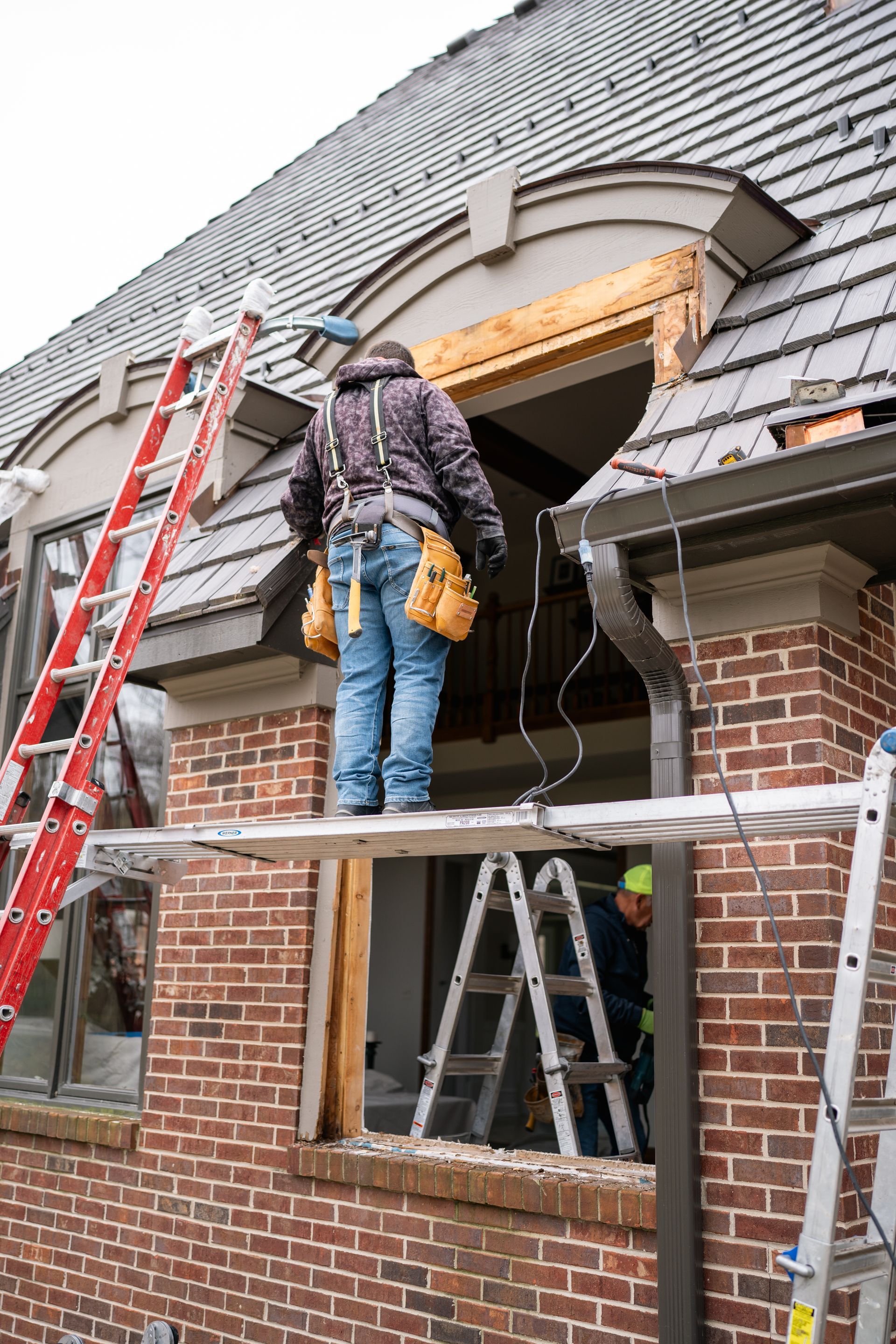 Construction worker on scaffold removing window, red brick building, ladder.