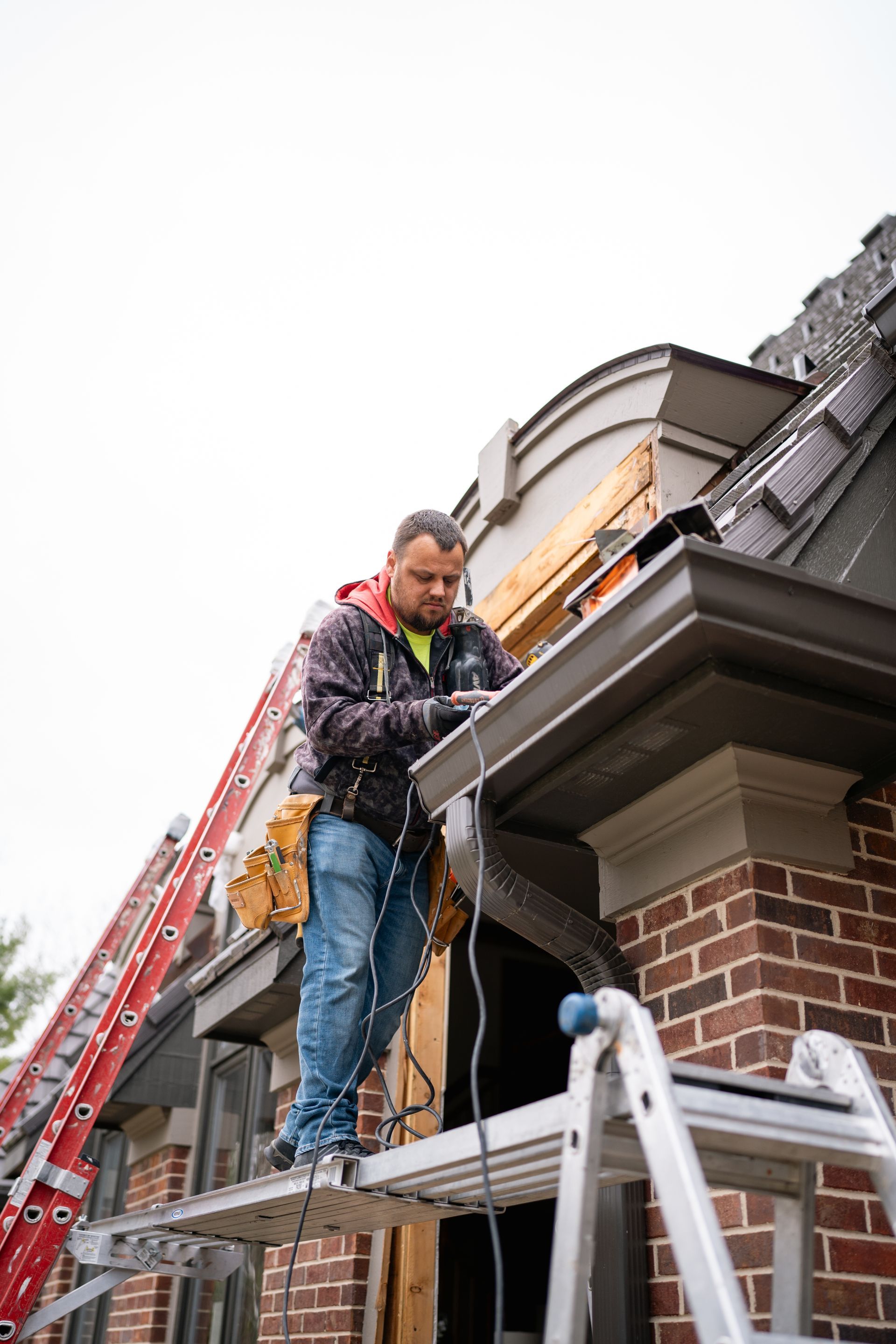 Construction worker on a ladder installing gutters on a brick house.