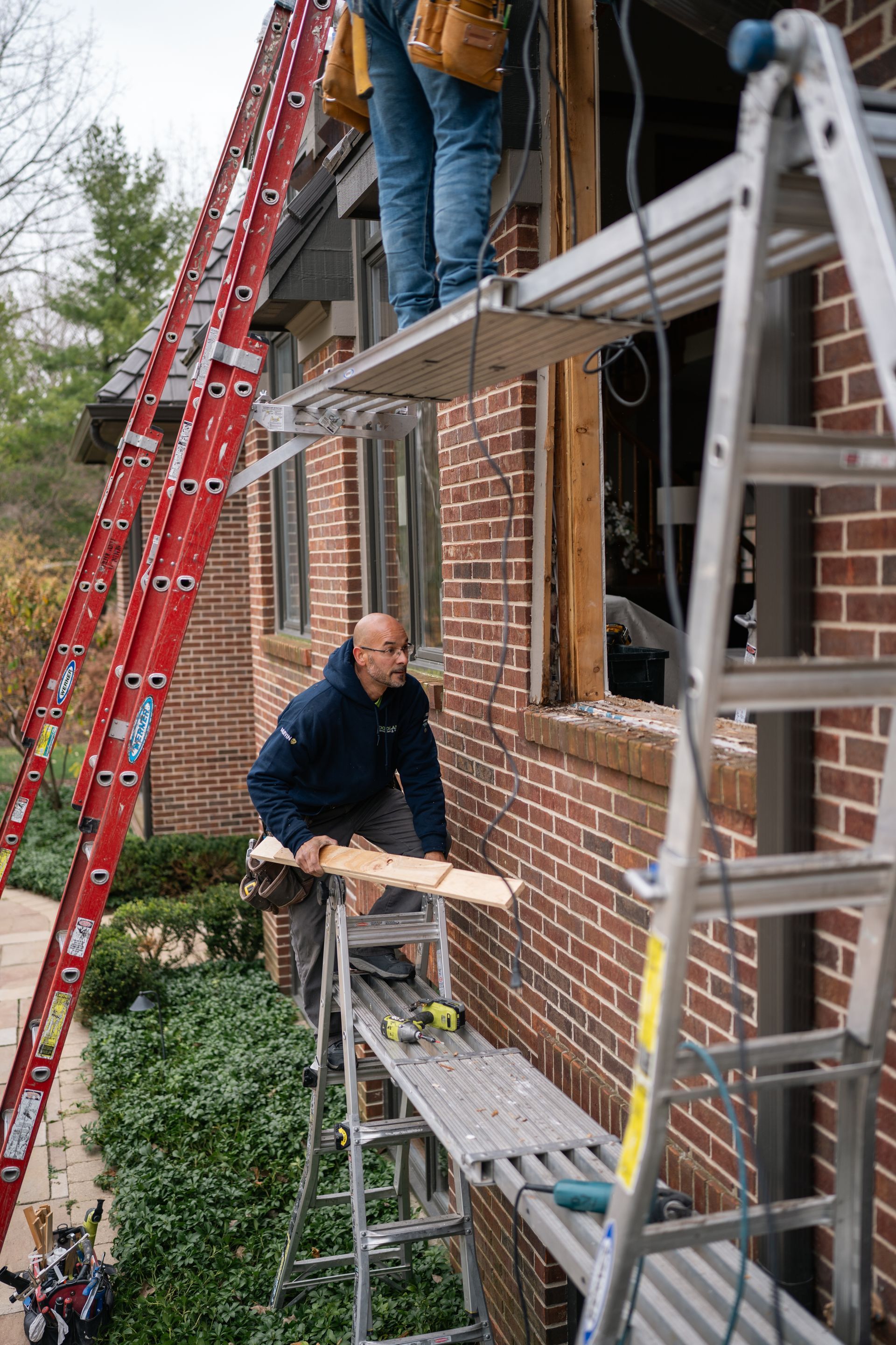 Construction workers installing window on a red brick building using ladders and scaffolding.