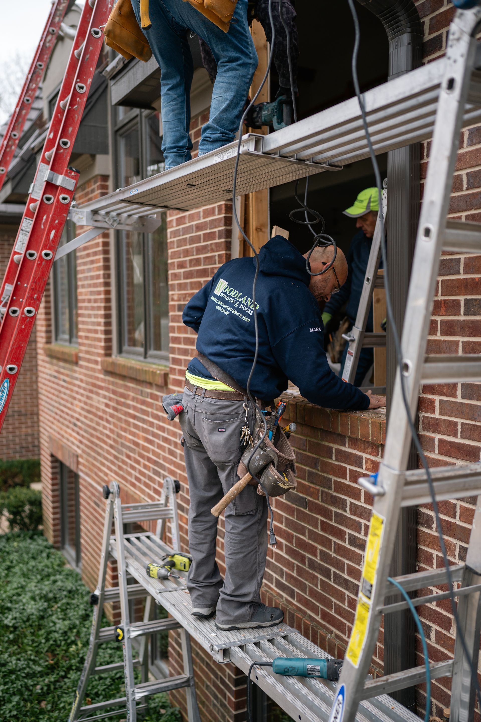 Construction workers replacing a window, standing on ladders and scaffolding, brick building.