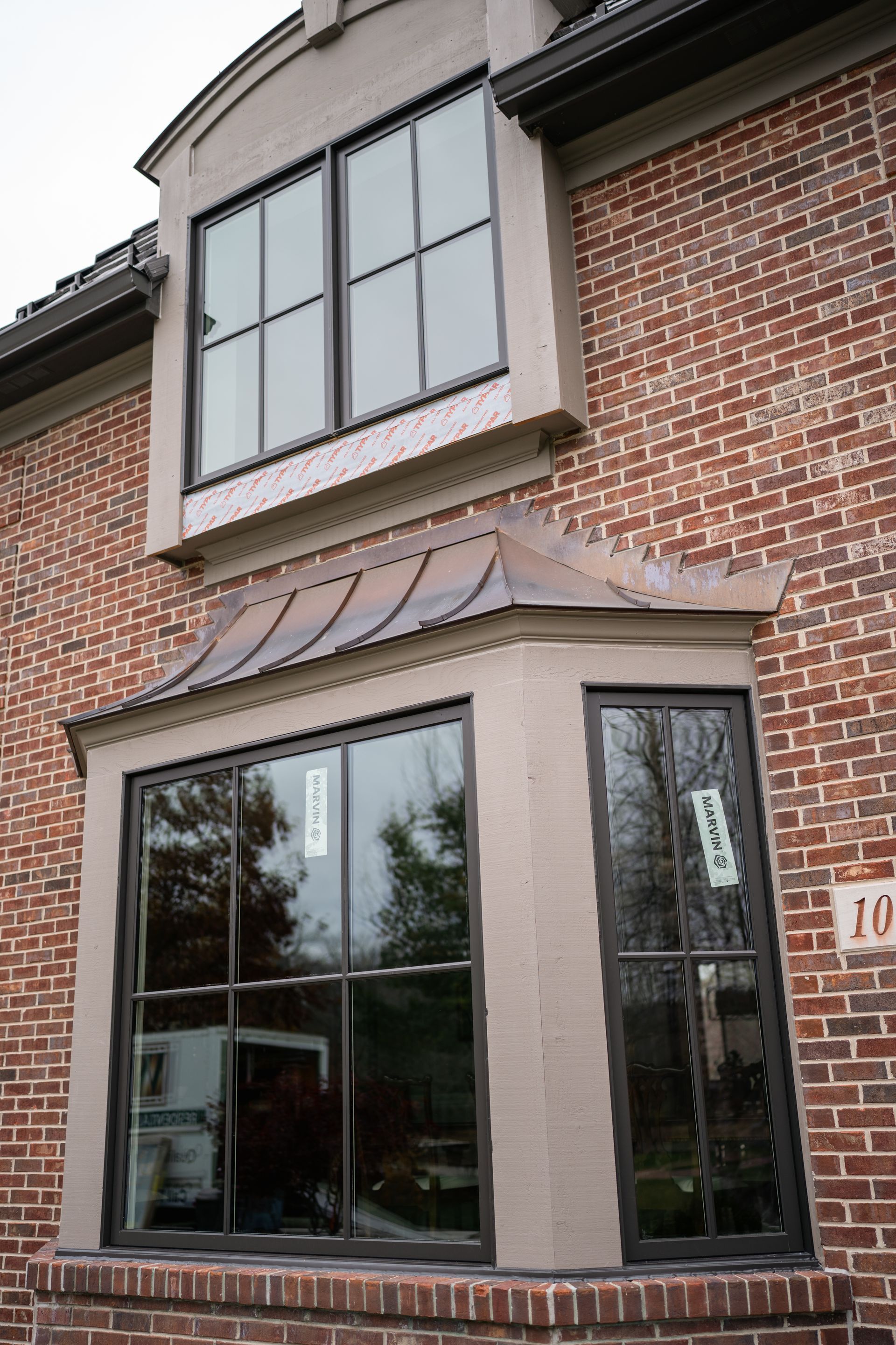 Brick building with dark-framed windows and a bay window with a copper roof.