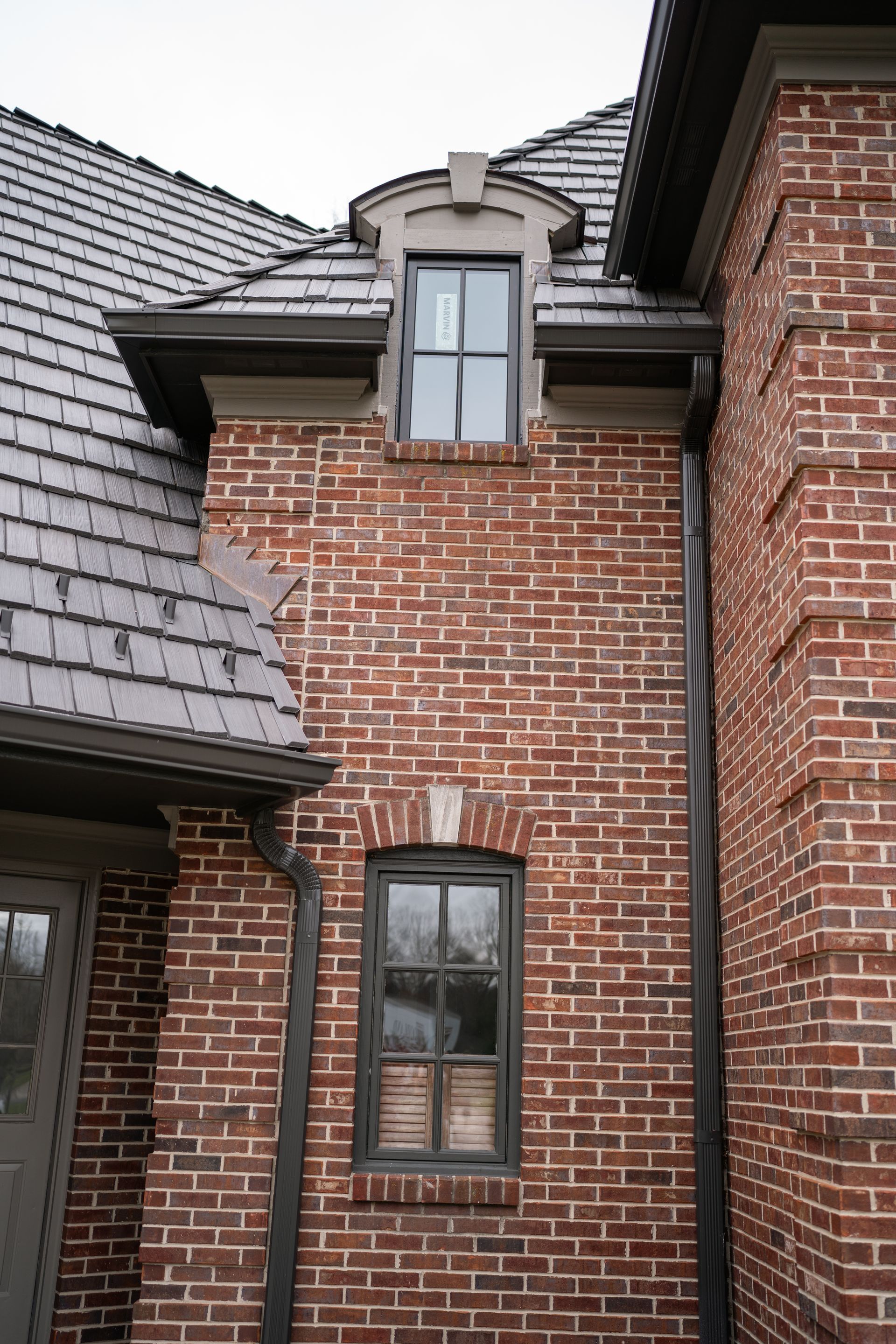 Red brick building with two windows and a gray shingled roof.