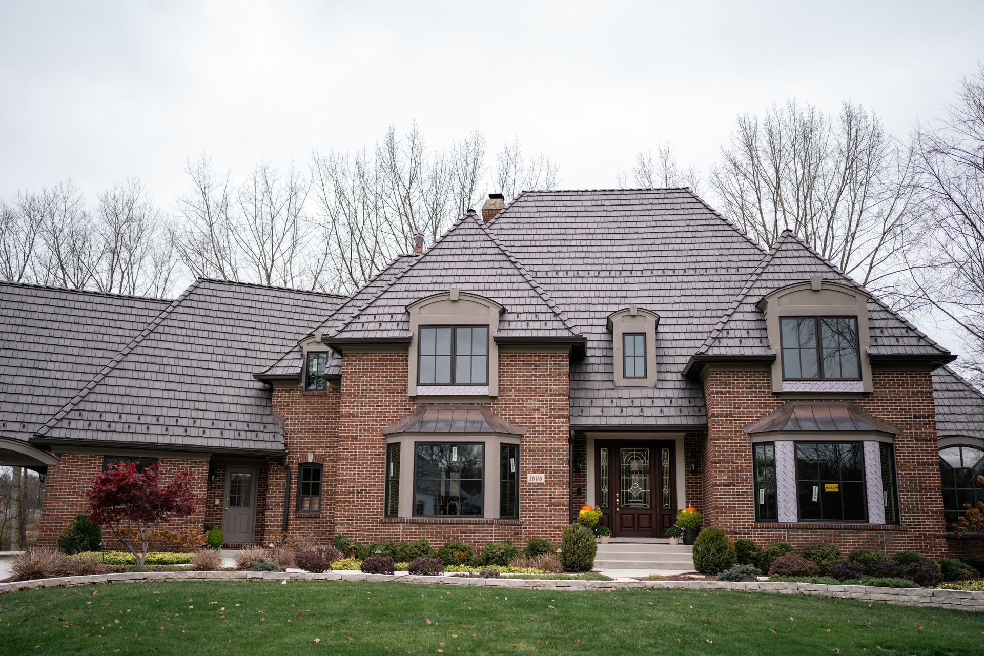 Brick home with gray roof, windows, and front lawn. Trees in the background under an overcast sky.