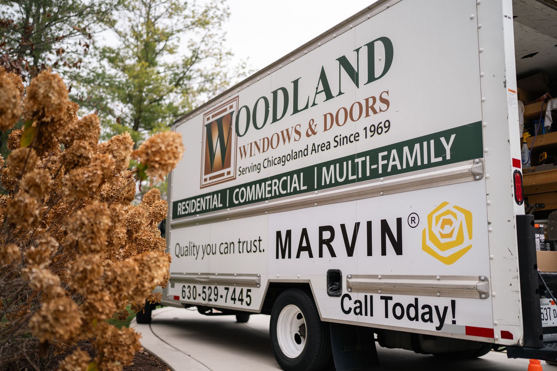 Woodland Windows & Doors truck, parked outdoors, near a brown bush.