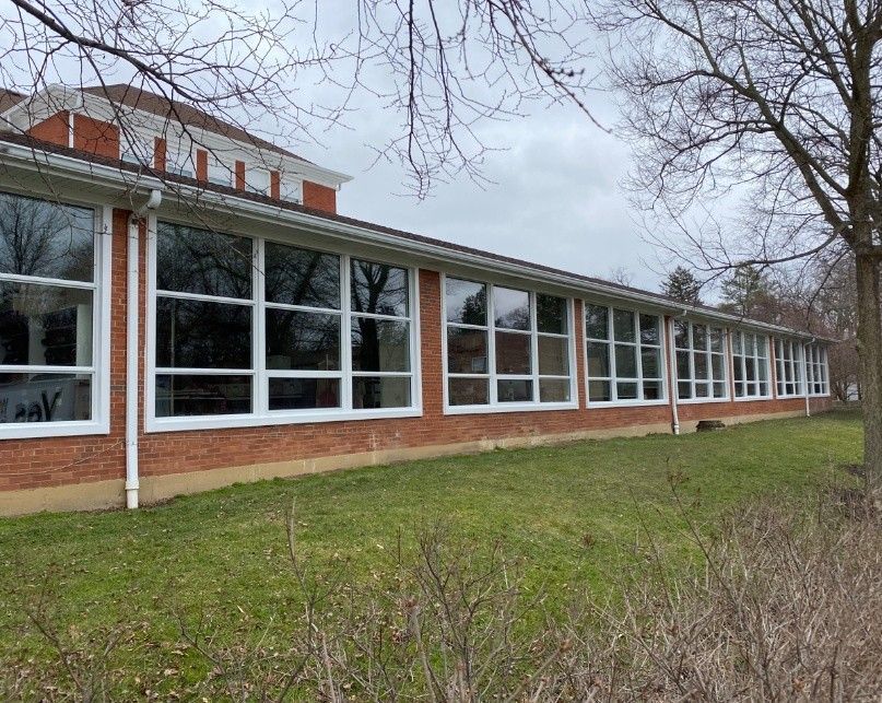 A two-story brick mansion with white columns, a large triangular pediment, and black shutters, set among trees and shrubs.