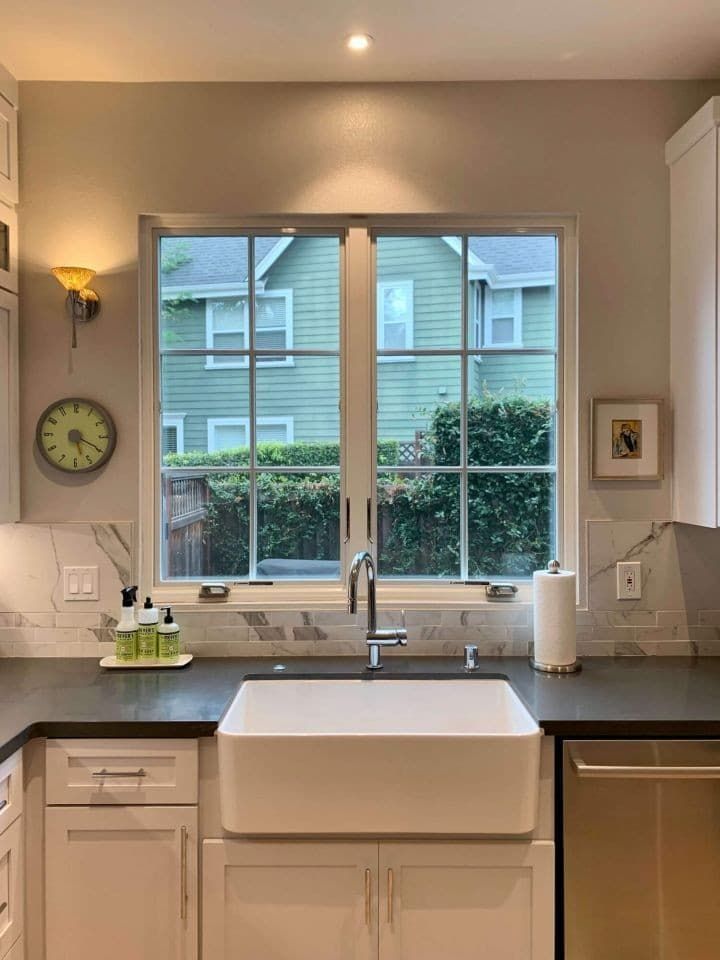 A kitchen with a sink and a window with a clock on the wall.