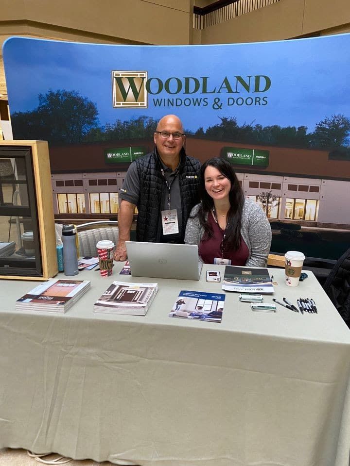 A man and a woman are standing at a woodland windows and doors booth.