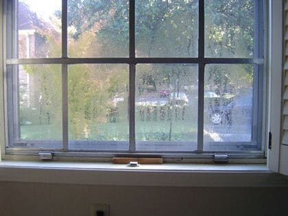 A window with a condensation on it and a view of a yard.