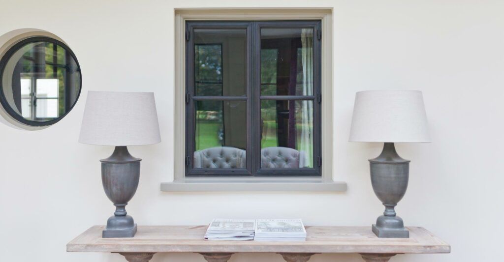 A table with two lamps and a book on it in front of a window.