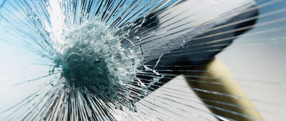 A hammer is breaking through a broken glass window.