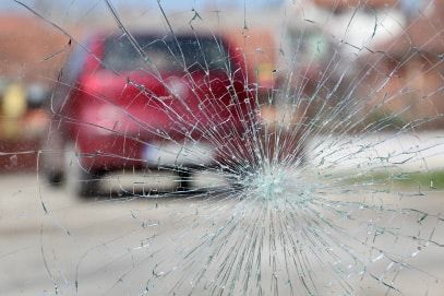 A red car is driving past a broken windshield.