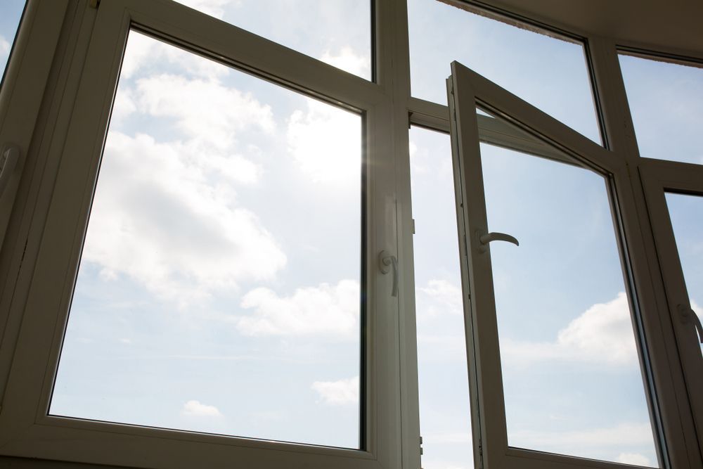Open window with white frame against a bright sky with scattered clouds.
