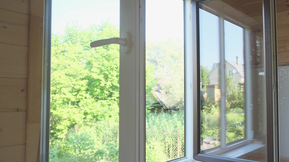 An open window with a view of a forest and a house in the background.