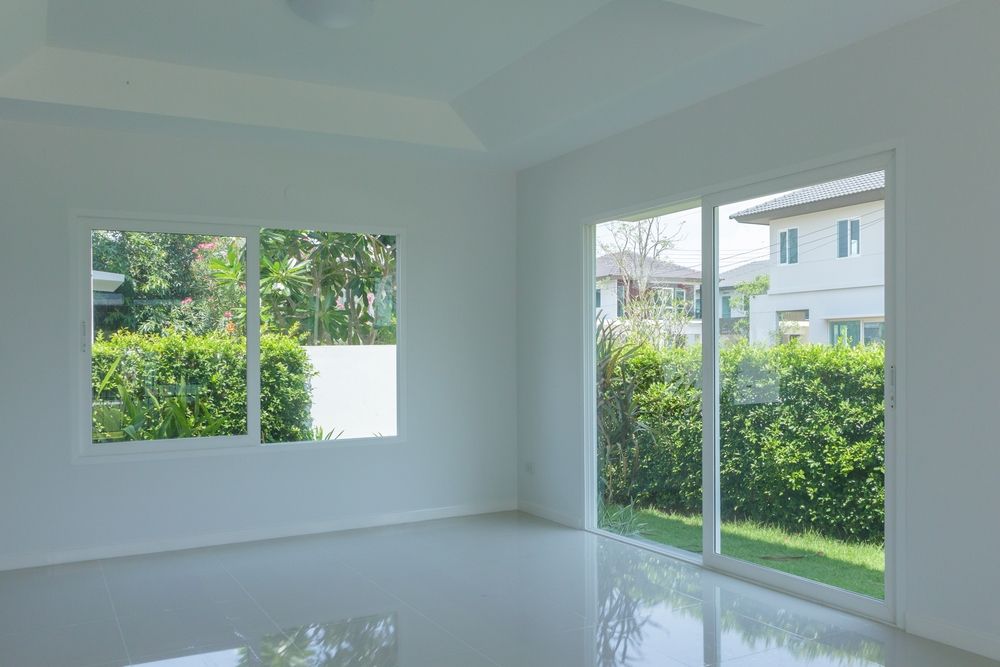 Empty white room with large windows overlooking greenery and houses.