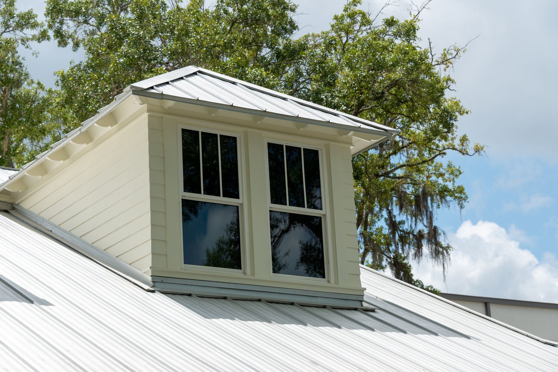 A white house with a metal roof and a window on the roof