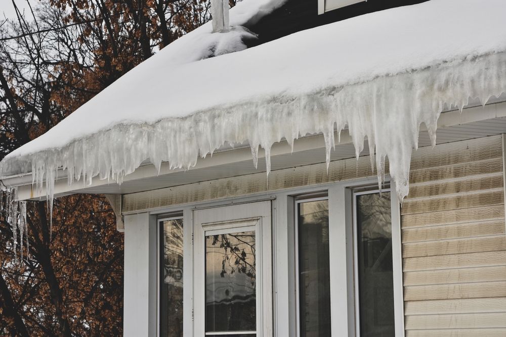 Roof covered in snow and long icicles hanging over windows.
