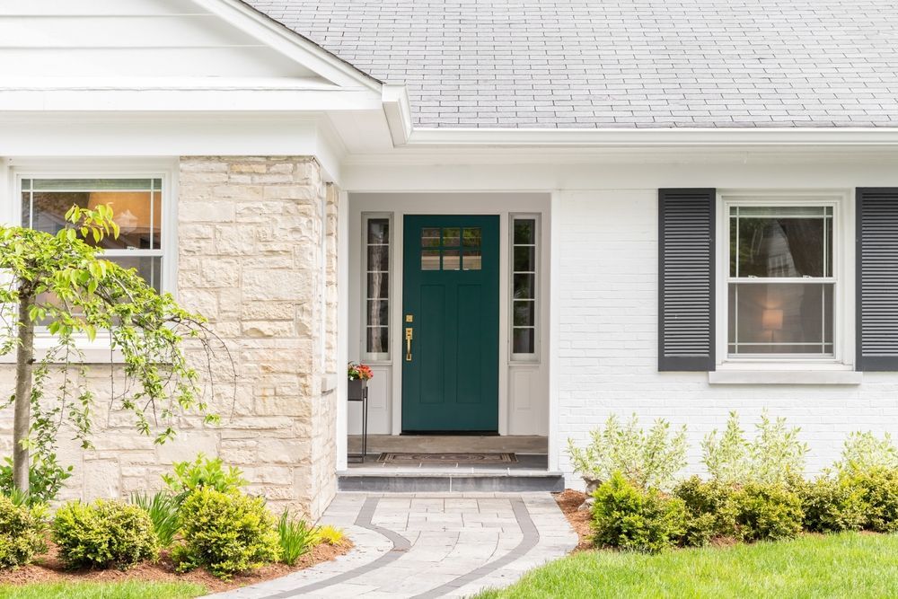 A white house with a green front door and black shutters.
