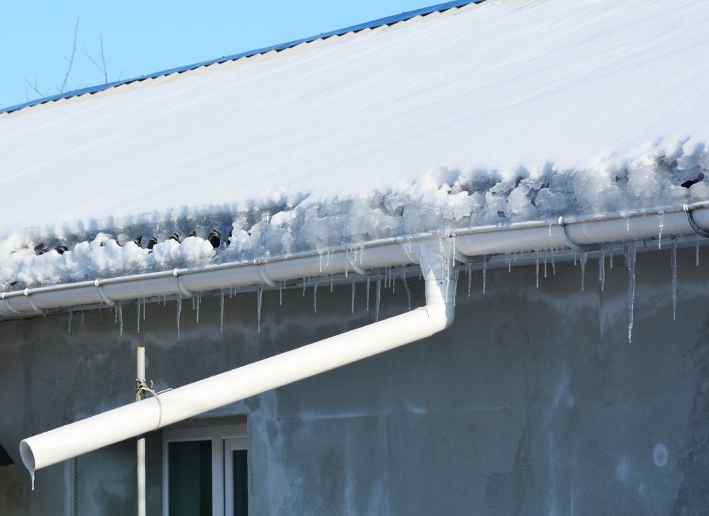 Snow and icicles on a roof gutter and downspout of a building on a sunny day.