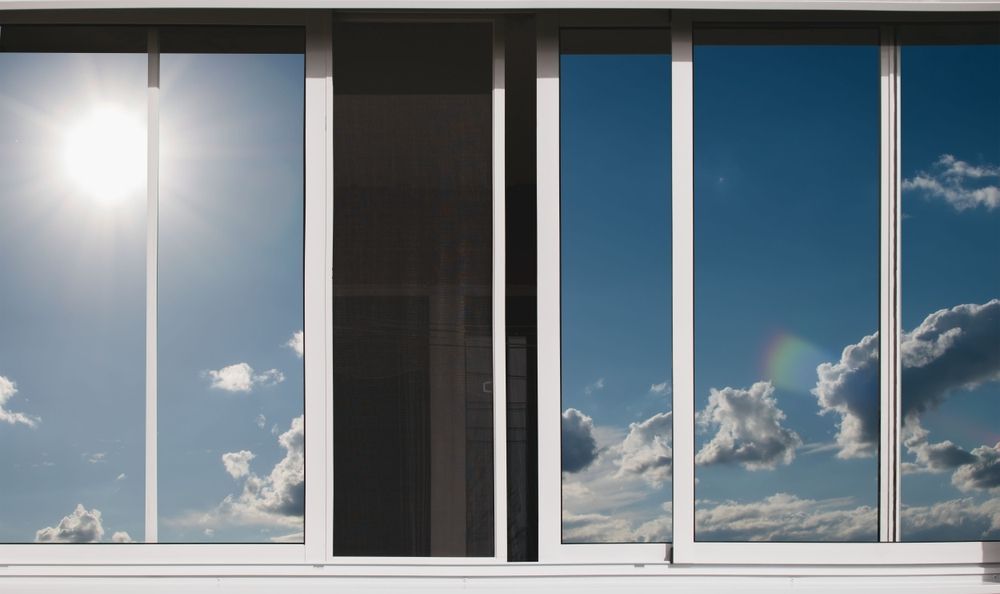 Sliding glass windows reflect a sunny sky with clouds.