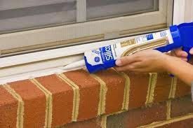 A person is applying caulk to a window sill on a brick wall.