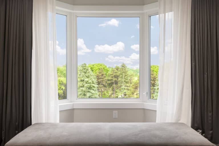 A bedroom with a large bay window and a bed in front of it.