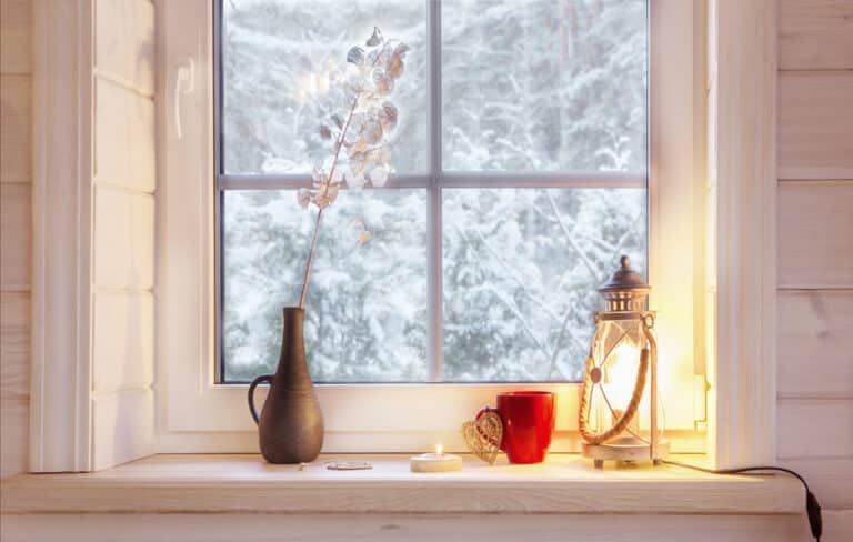 A window sill with a vase , cup , candle and lantern on it.