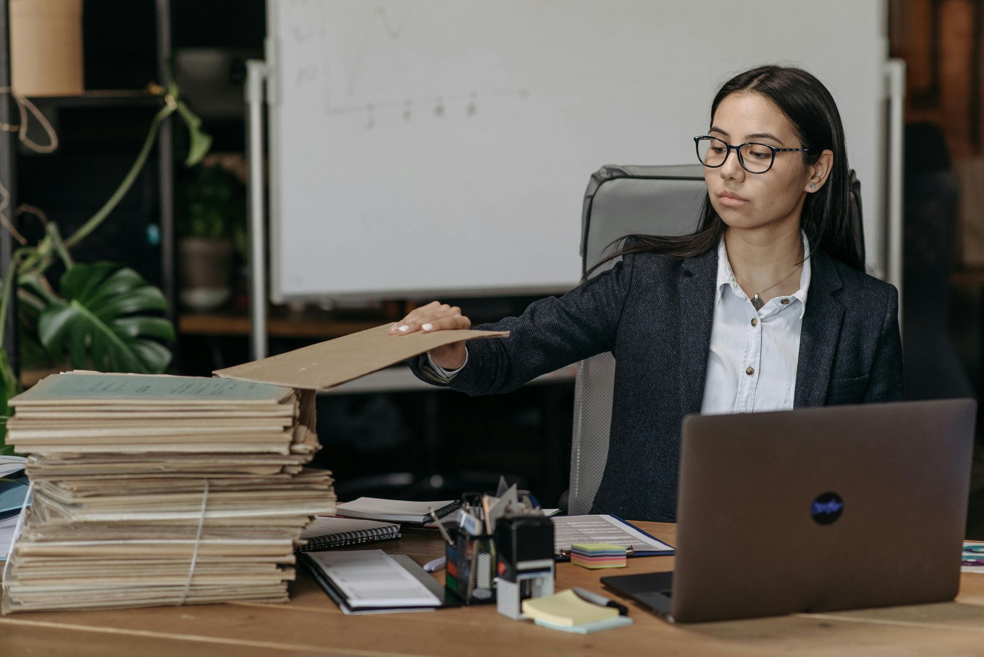 A professional seated at a desk, looking at a large stack of documents while placing a folder on top of it.