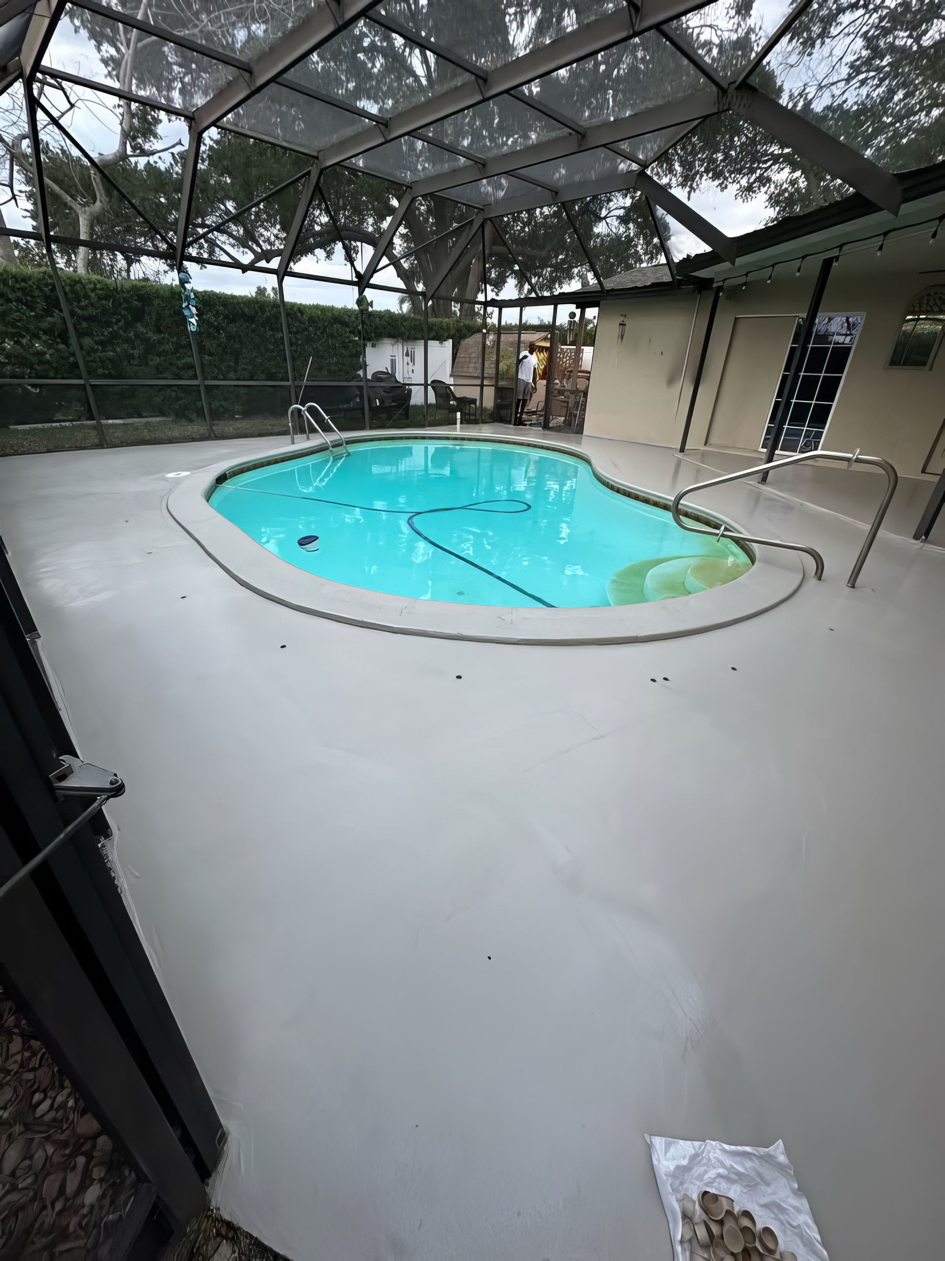 Indoor-outdoor pool under a screened patio with light blue water and white deck, surrounded by greenery