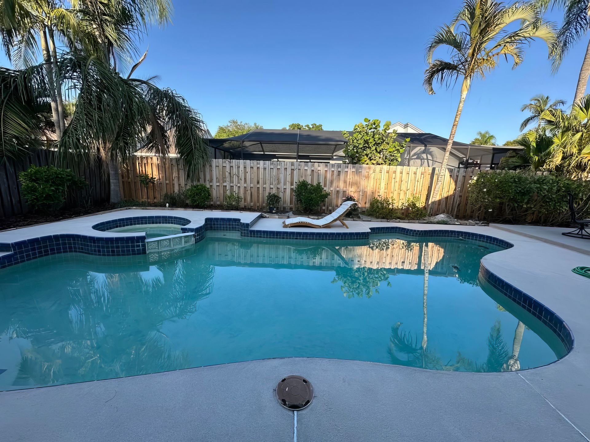Backyard swimming pool with turquoise water, white deck, palm trees, and lounge chairs at sunset