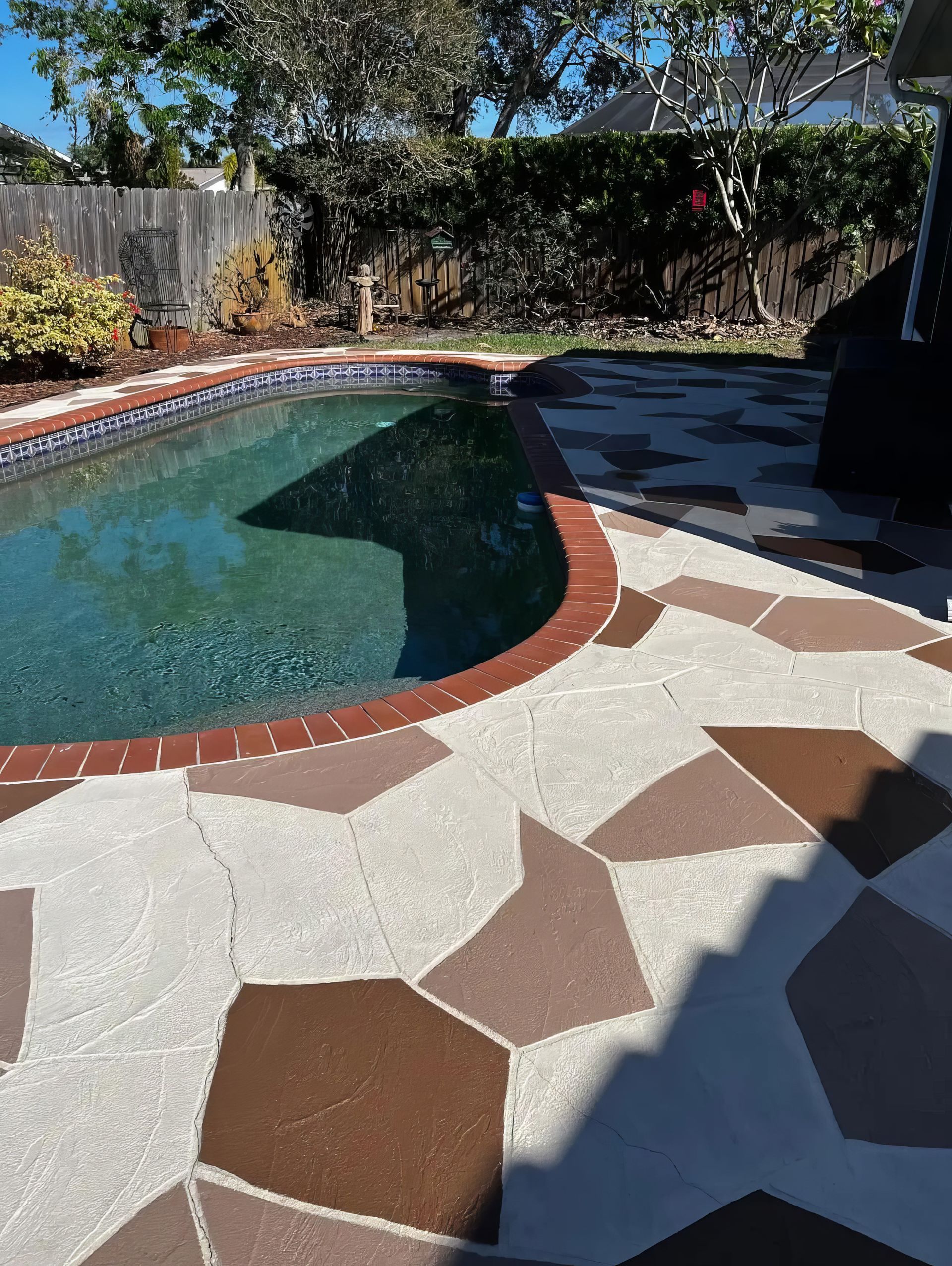 Backyard swimming pool with patterned patio tiles and trees in the background