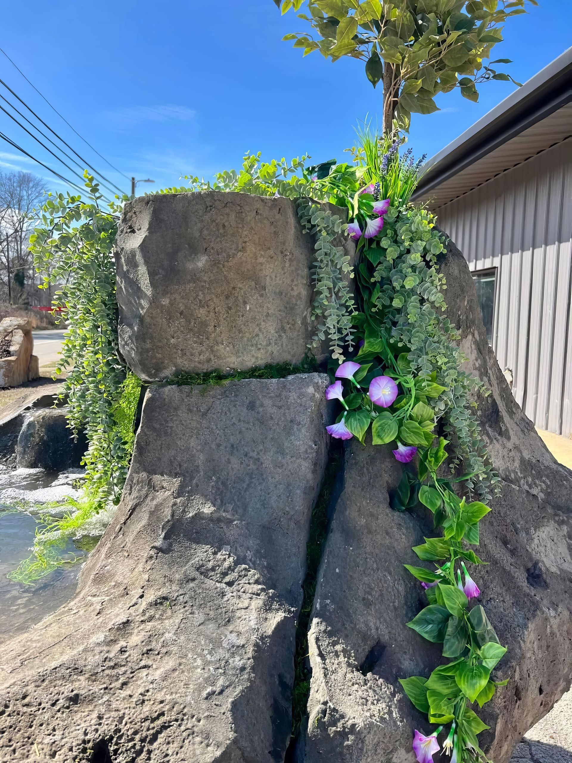 Stone sculpture with purple flowers and green vines against a blue sky