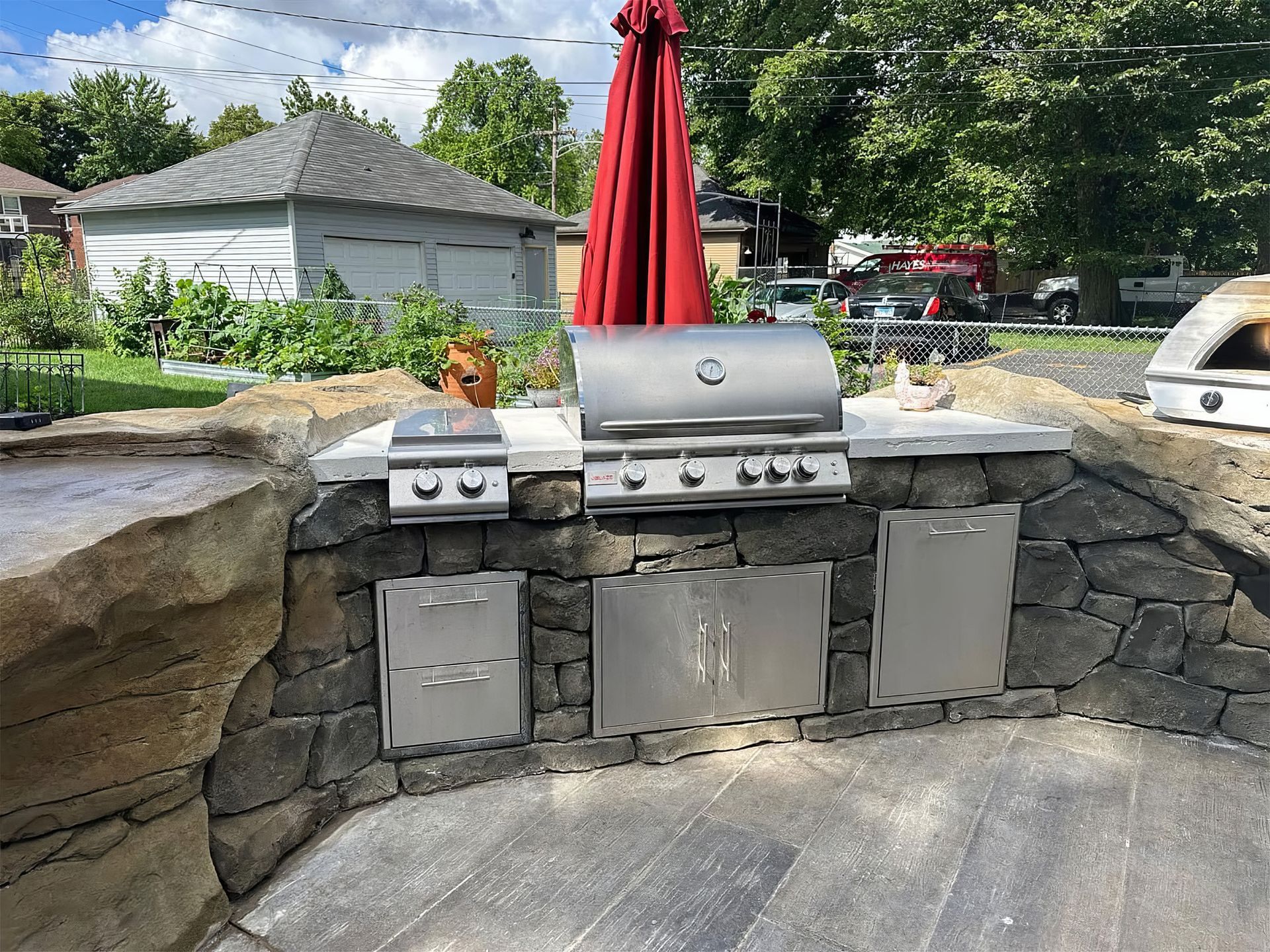 Outdoor stone patio with stainless steel grill, red umbrella, and stone wall seating area