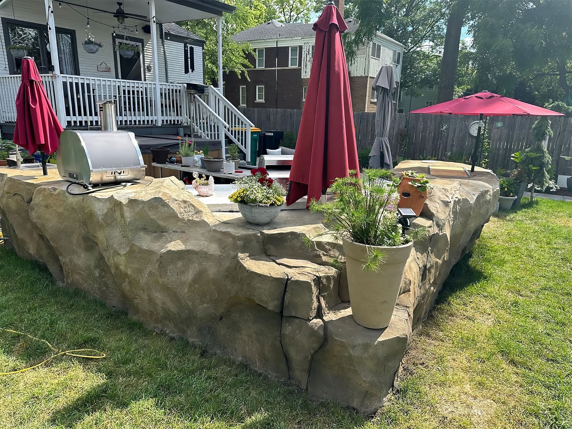 Backyard stone patio with red umbrellas, potted plants, and a white house porch in the background