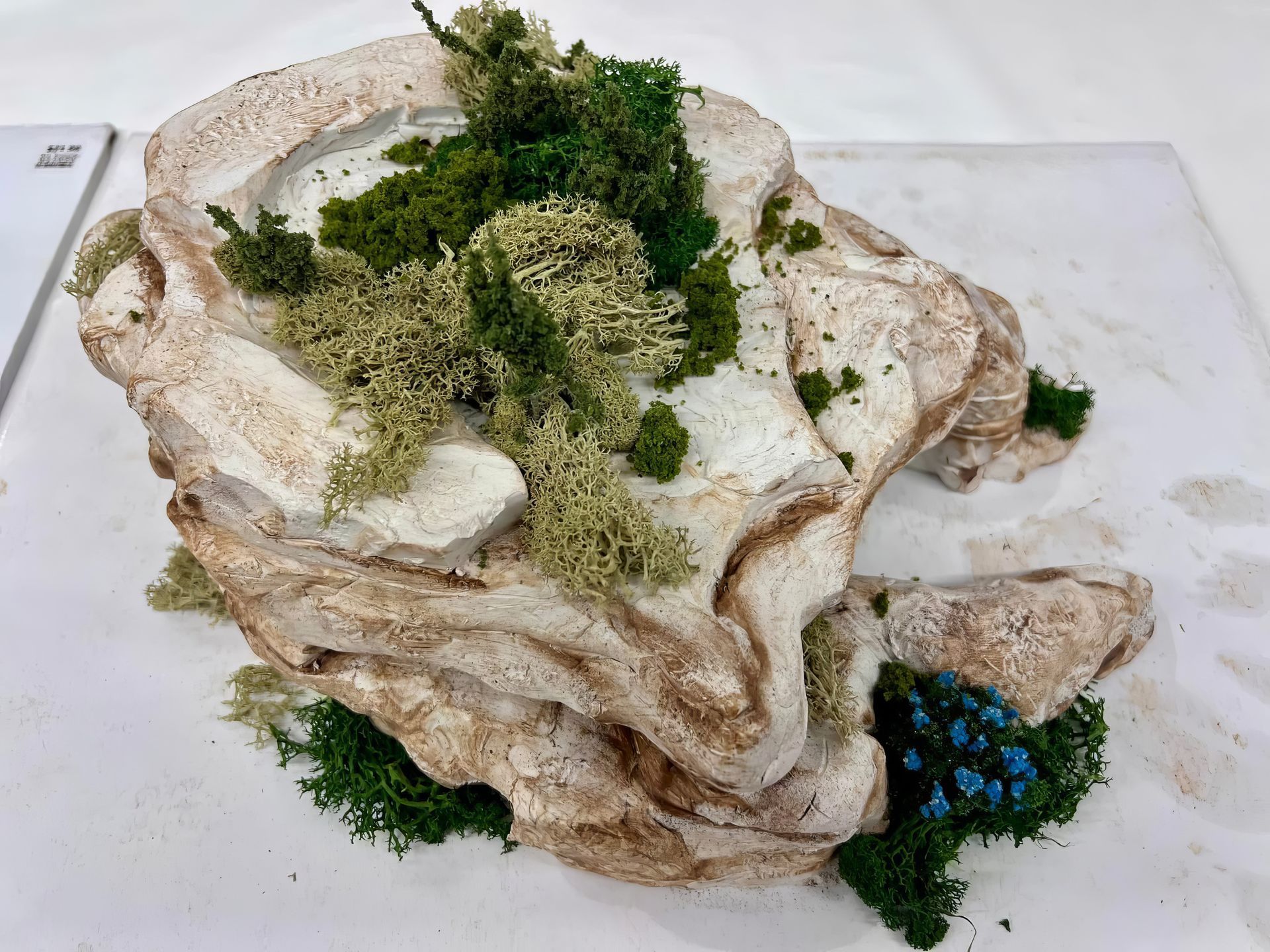 Miniature rock formation with moss and small blue flowers on a white background