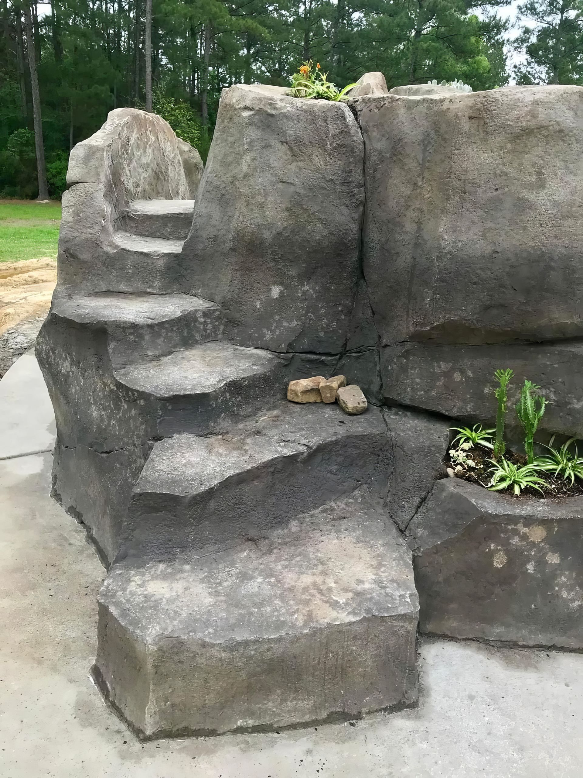 Stone steps built into a faux rock wall beside a garden path and plants