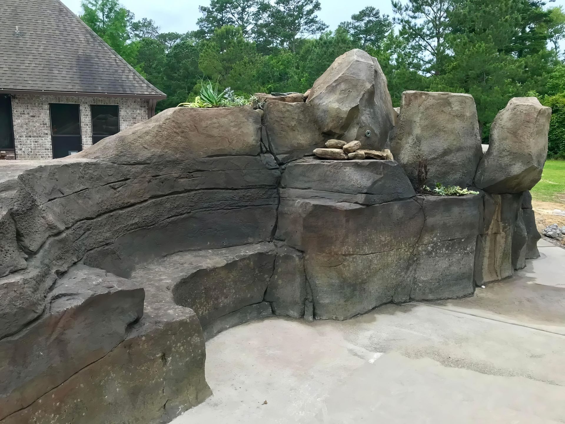 Large gray rock formation in an outdoor zoo-like enclosure with trees and a thatched structure in the background