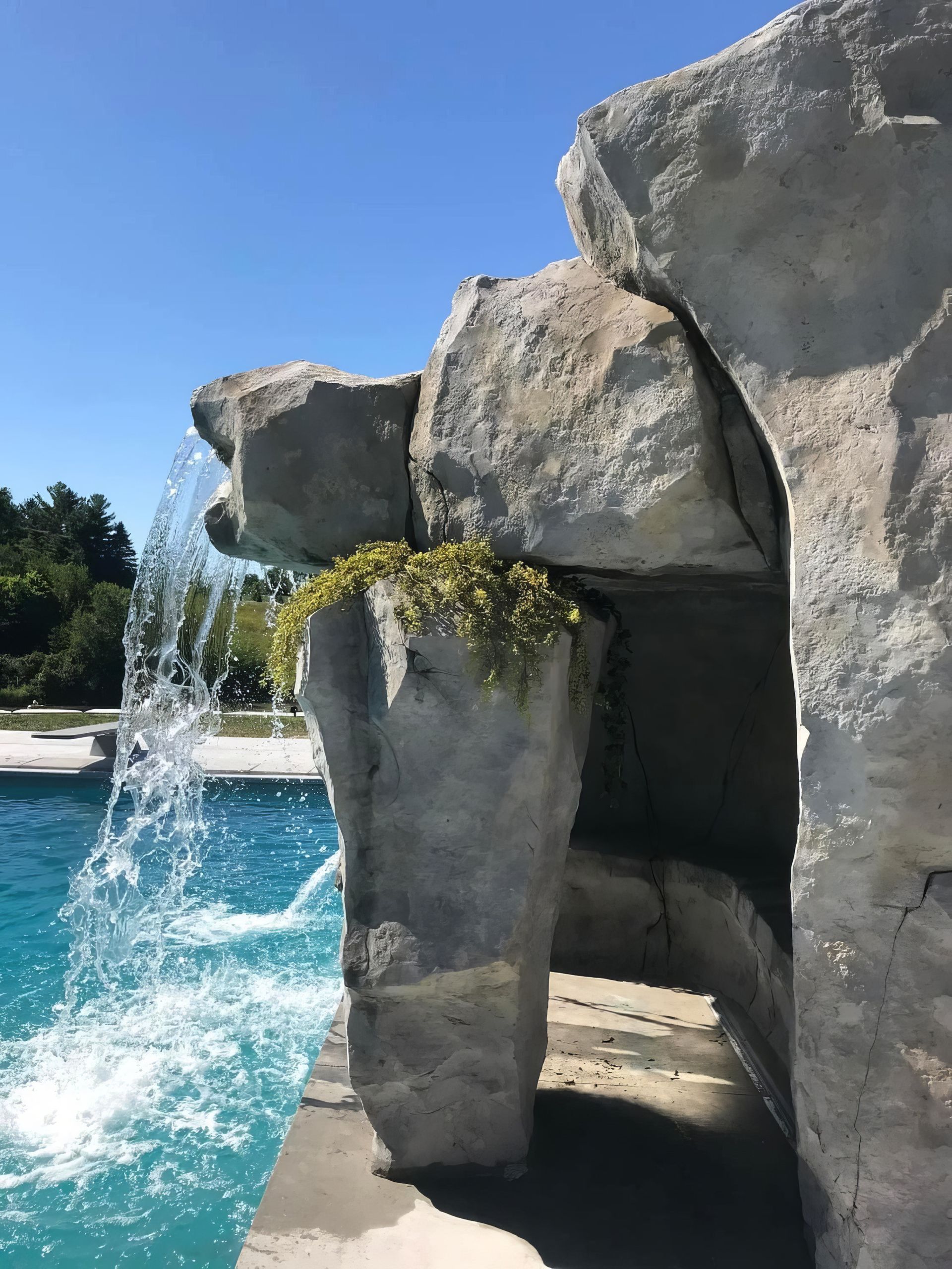 Rock waterfall pouring into a bright blue pool beside a stone grotto entrance