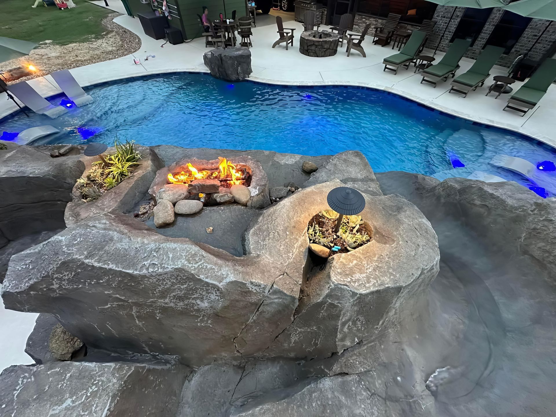 Curved resort pool with a stone fire pit centerpiece and lounge chairs along the deck