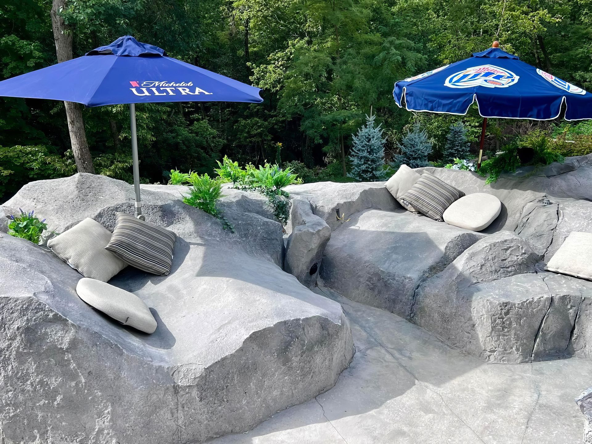 Two blue umbrellas shading gray stone lounge rocks in a garden setting
