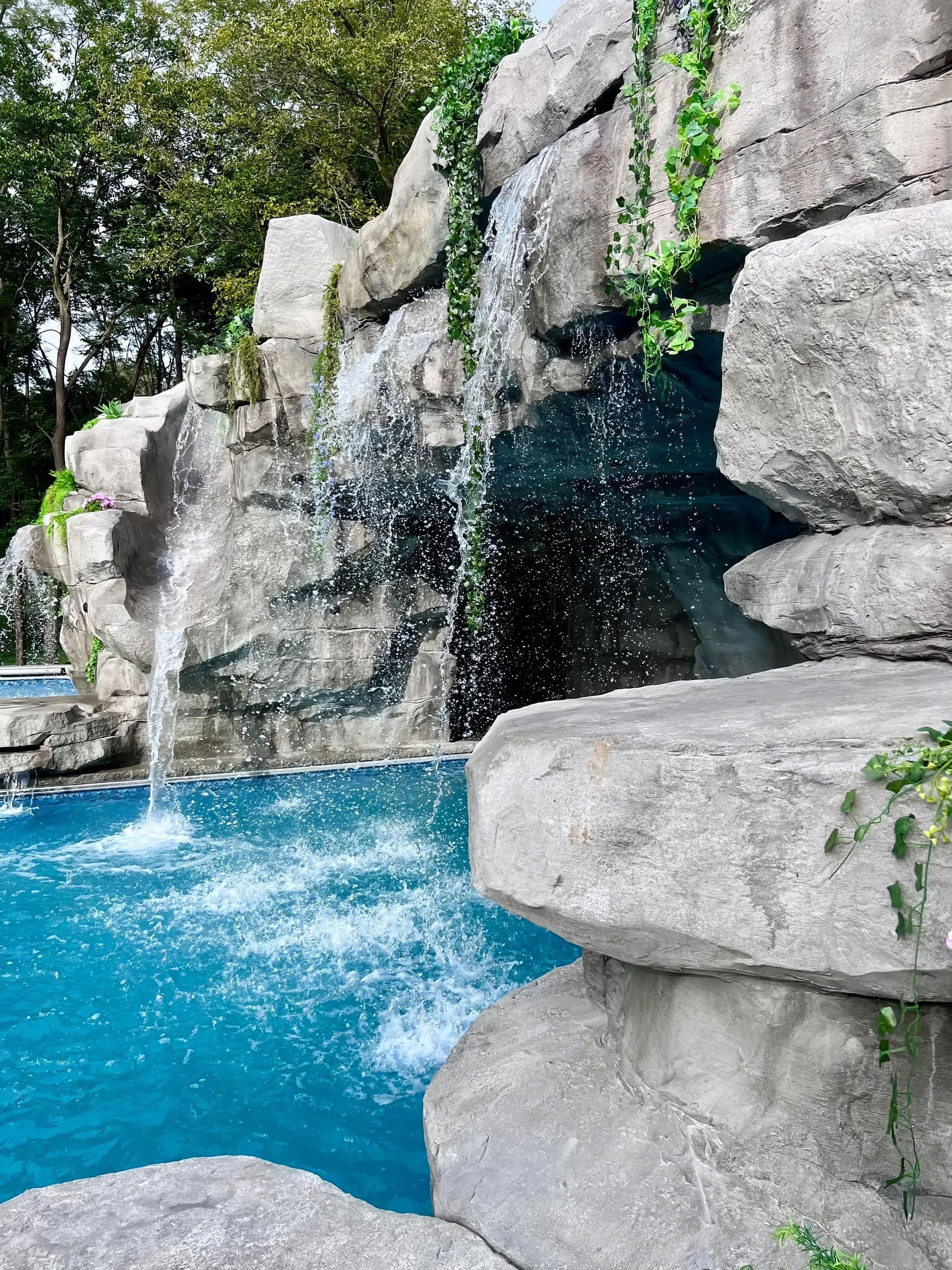 Rock waterfall cascading into a bright blue pool beside large gray stones and green foliage