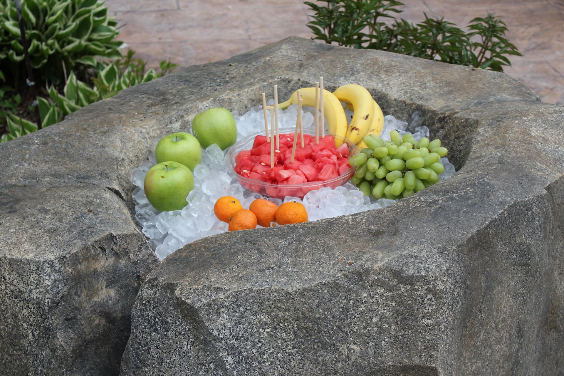 Assorted fruit arranged in a stone basin filled with ice outdoors.