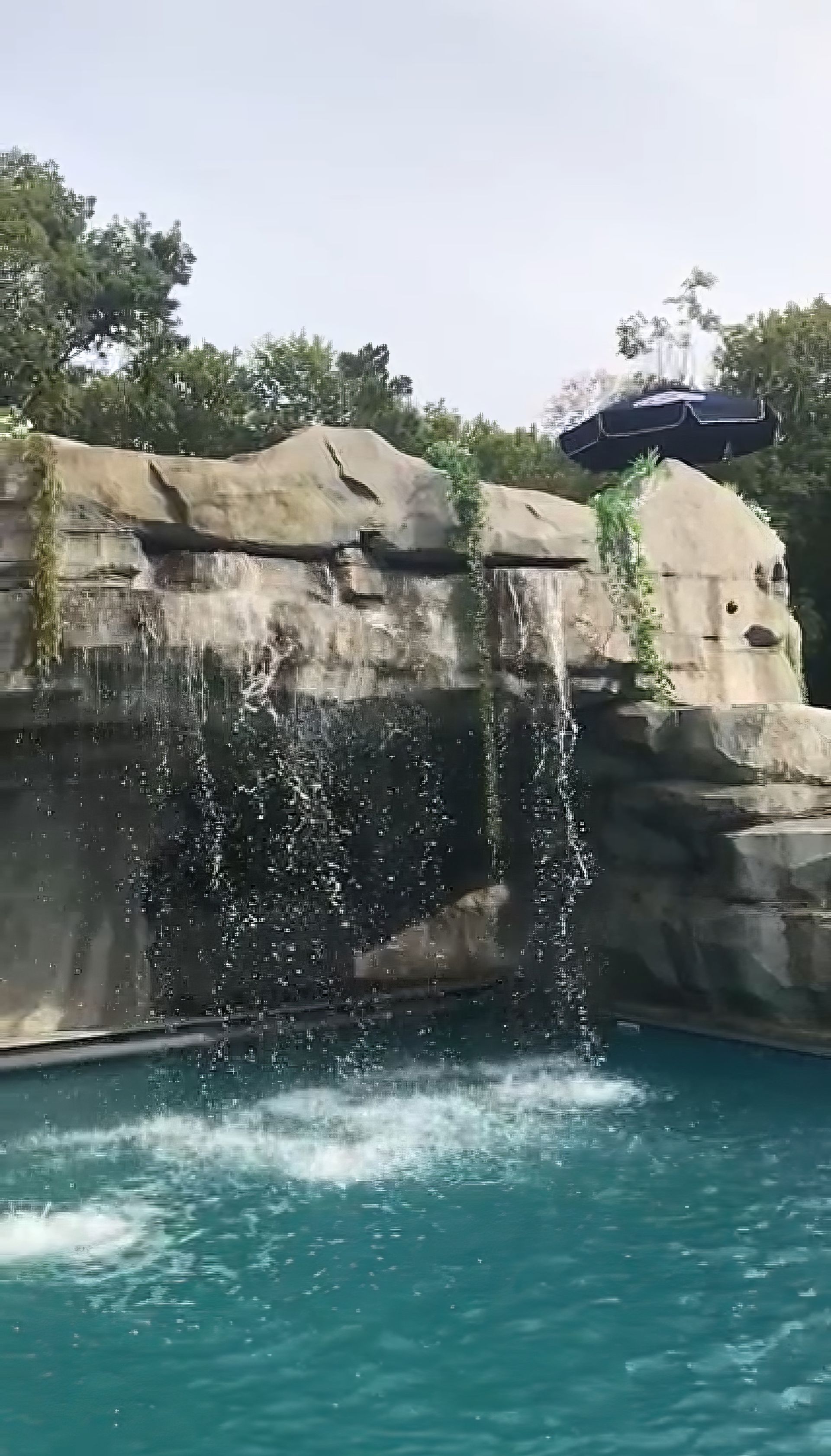 Waterfall spilling from a rocky ledge into a turquoise pool, with trees above.