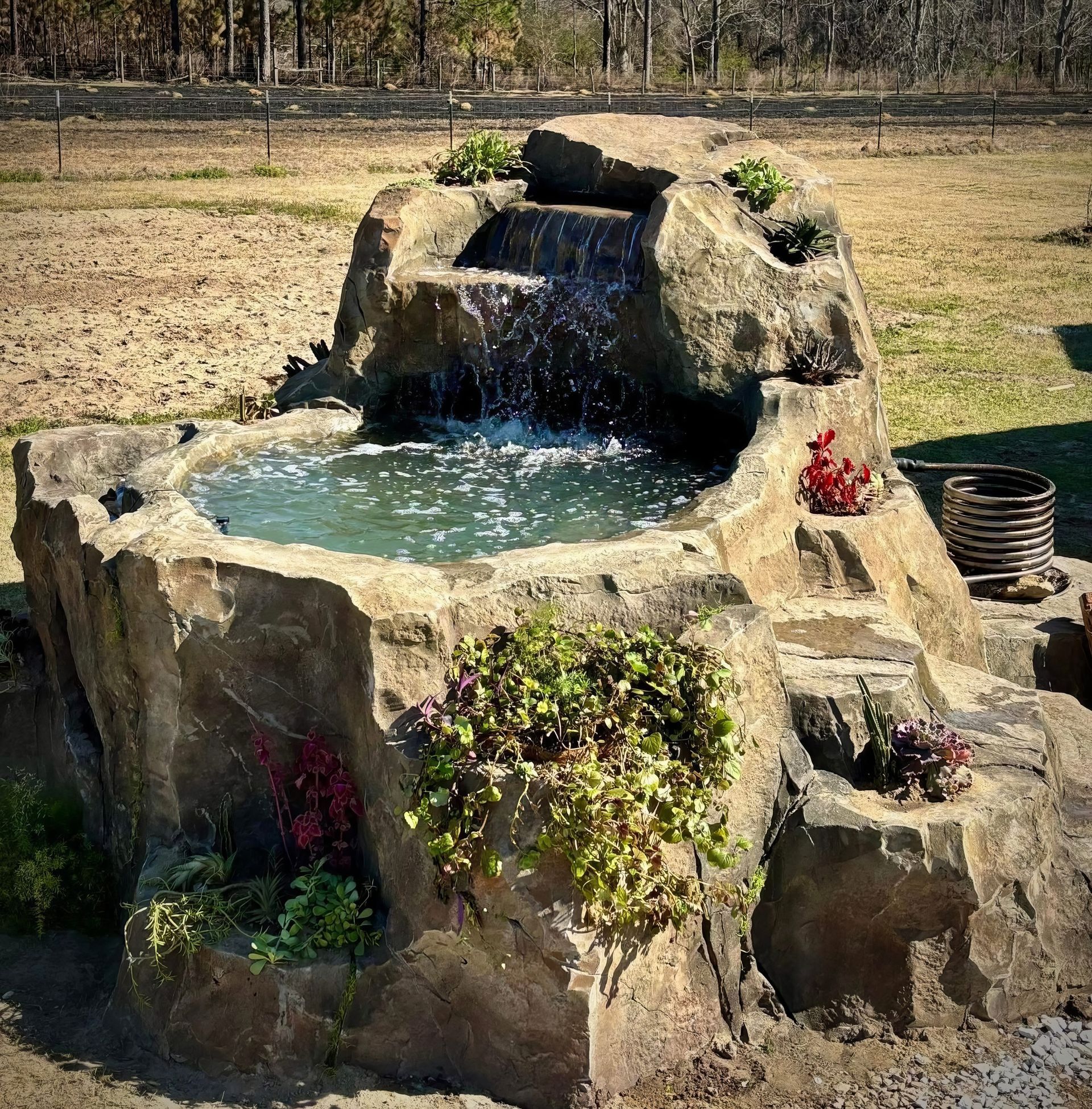 Stone garden fountain with flowing water and small plants around it